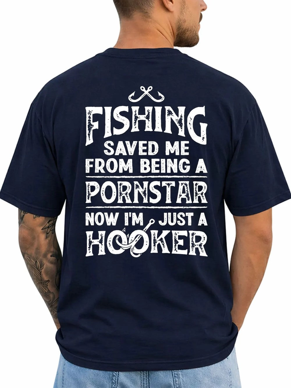 A man shown from the back wearing a navy blue t-shirt with a humorous white graphic text print that reads 'FISHING SAVED ME FROM BEING A PORNSTAR NOW I'M JUST A HOOKER' accompanied by fishing hooks and line illustrations.