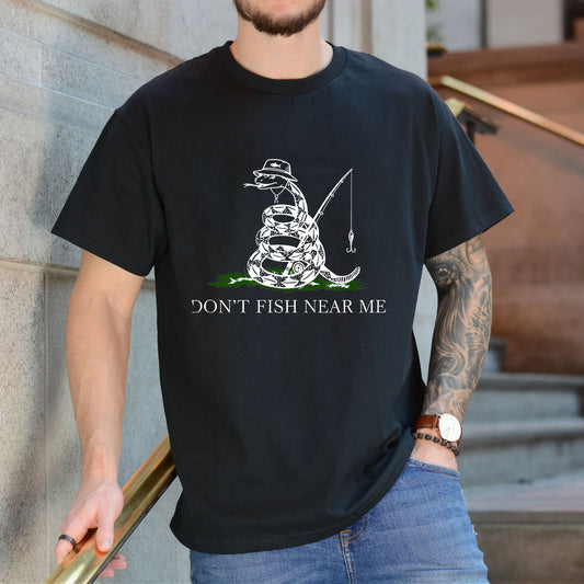Black T-shirt front with coiled snake angler holding a fishing rod and lure reading 'DON'T FISH NEAR ME'