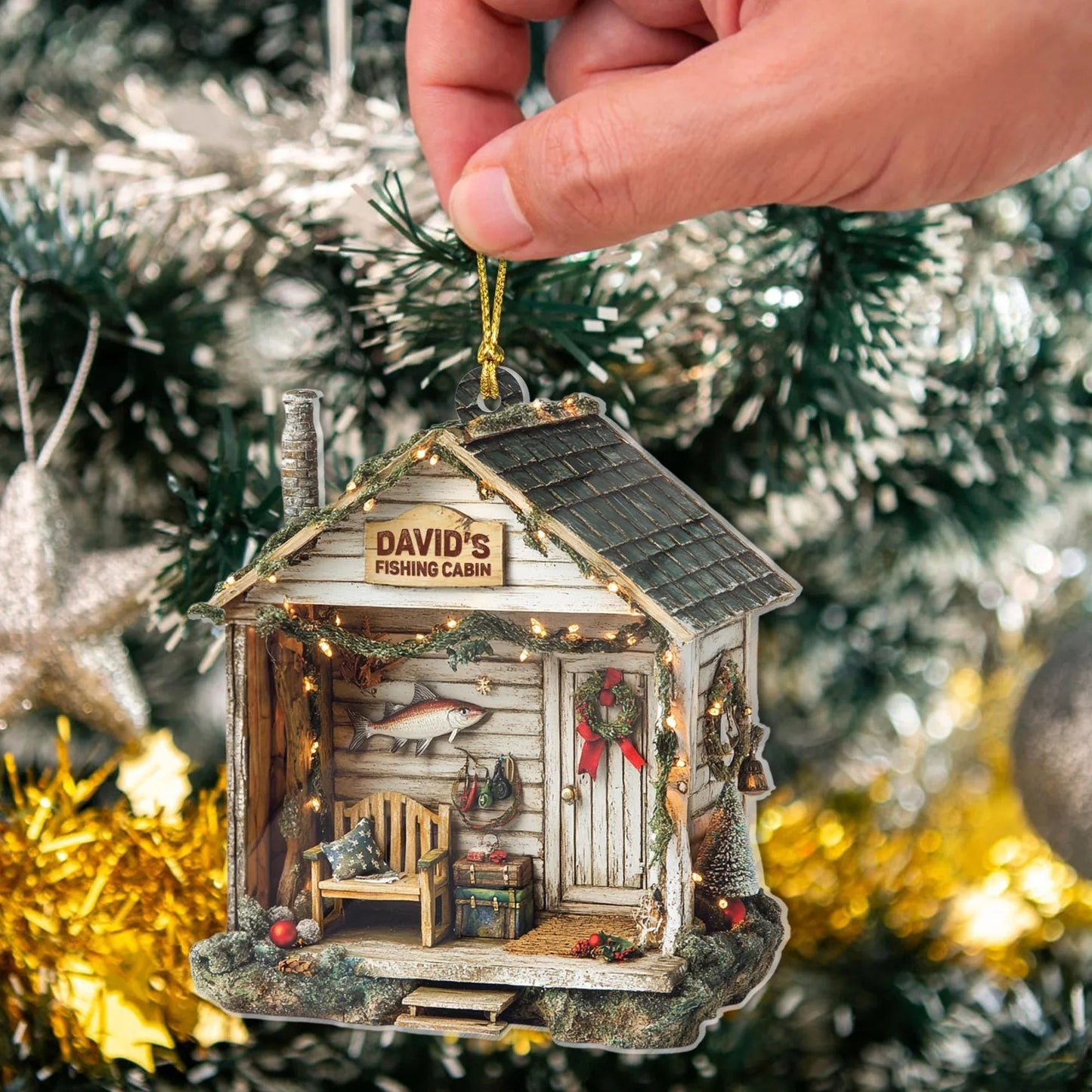 Hand holding a personalized fishing cabin ornament on a Christmas tree