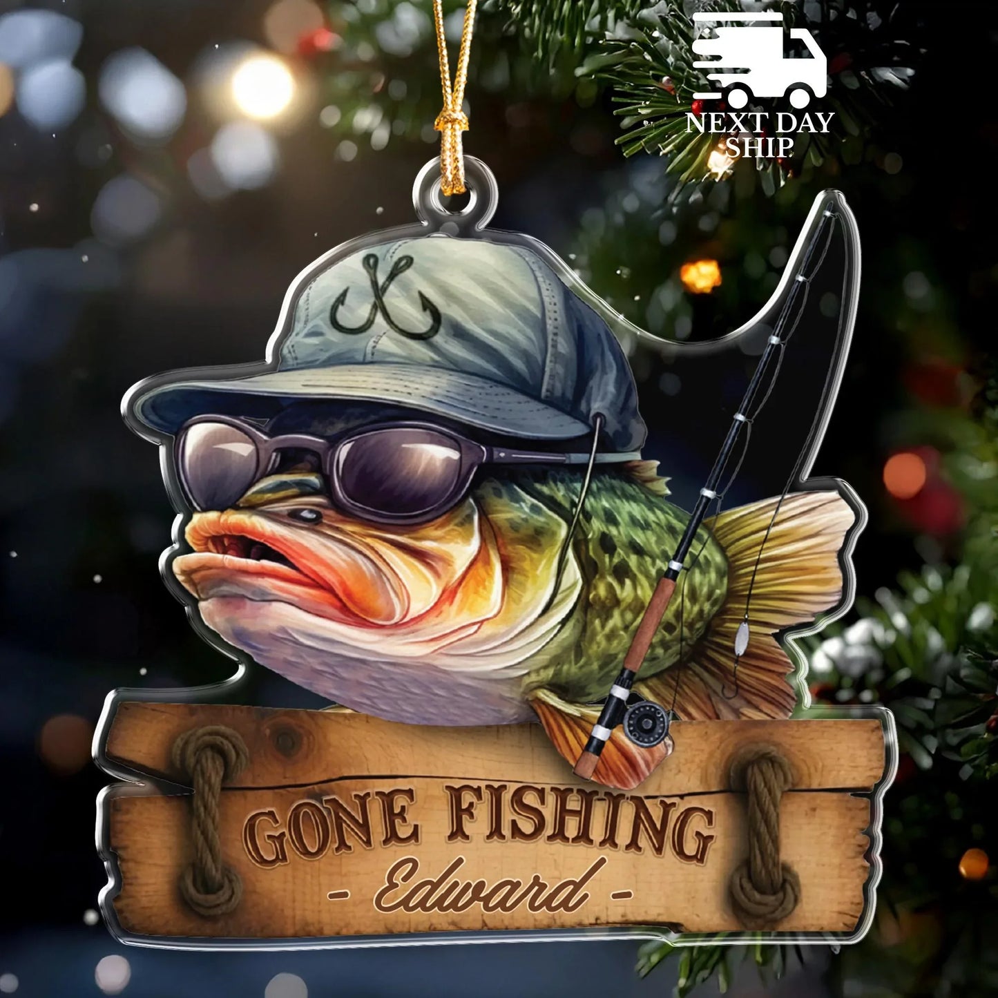 A personalized Christmas ornament shaped like a fishing scene, featuring a fish wearing a cap and sunglasses, a fishing rod, and a wooden sign that reads “GONE FISHING - Edward -”. The ornament is shown hanging against a blurred Christmas tree background with lights, and a “NEXT DAY SHIP” badge appears in the top right corner.
