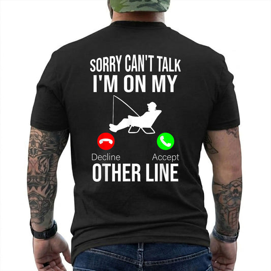 Black T-shirt back with seated angler, fishing line, and phone-call Other Line joke reading 'SORRY CAN'T TALK I'M ON MY OTHER LINE'